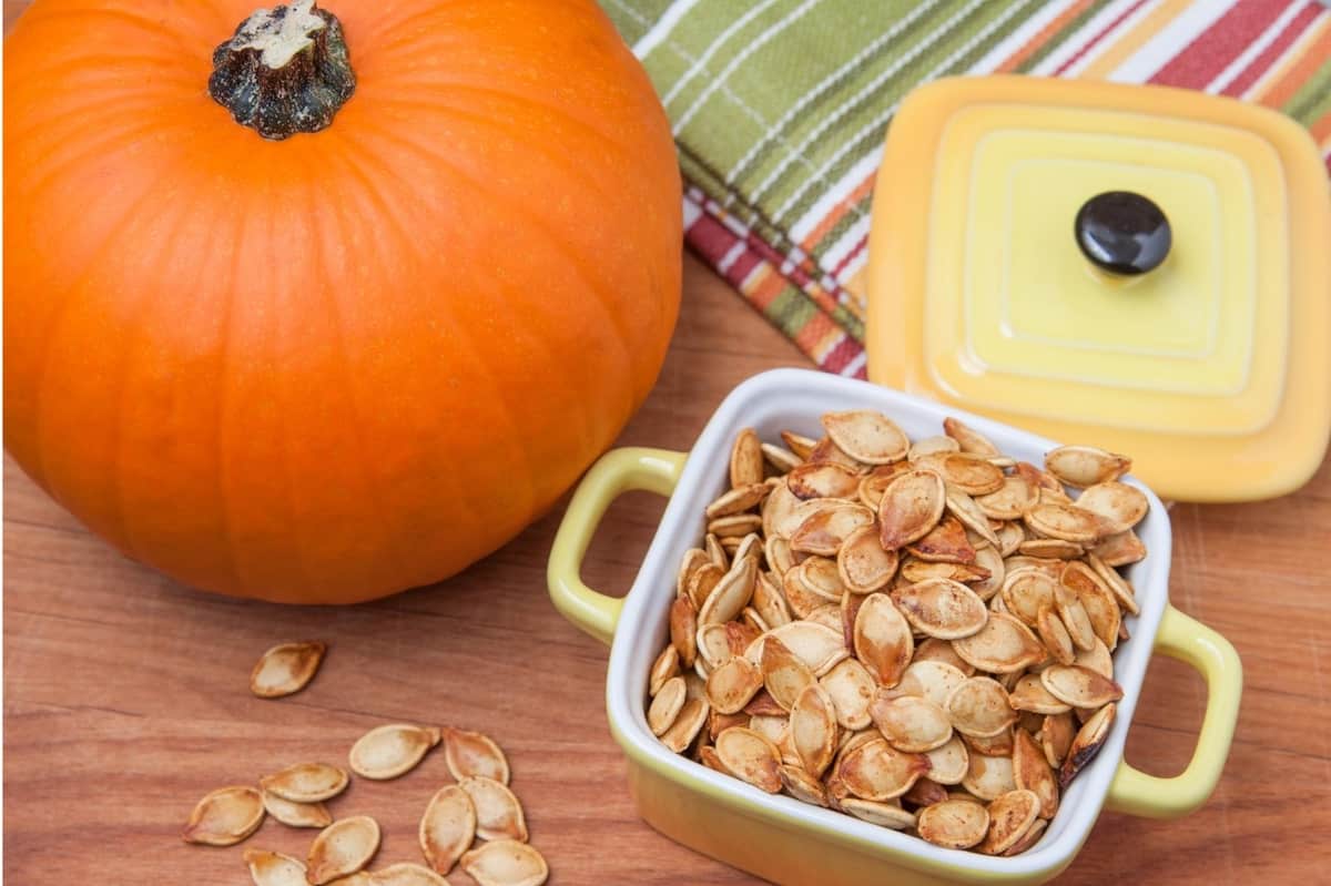 roasted pumpkin seeds in small bowl with pumpkin in background for pumpkin recipes
