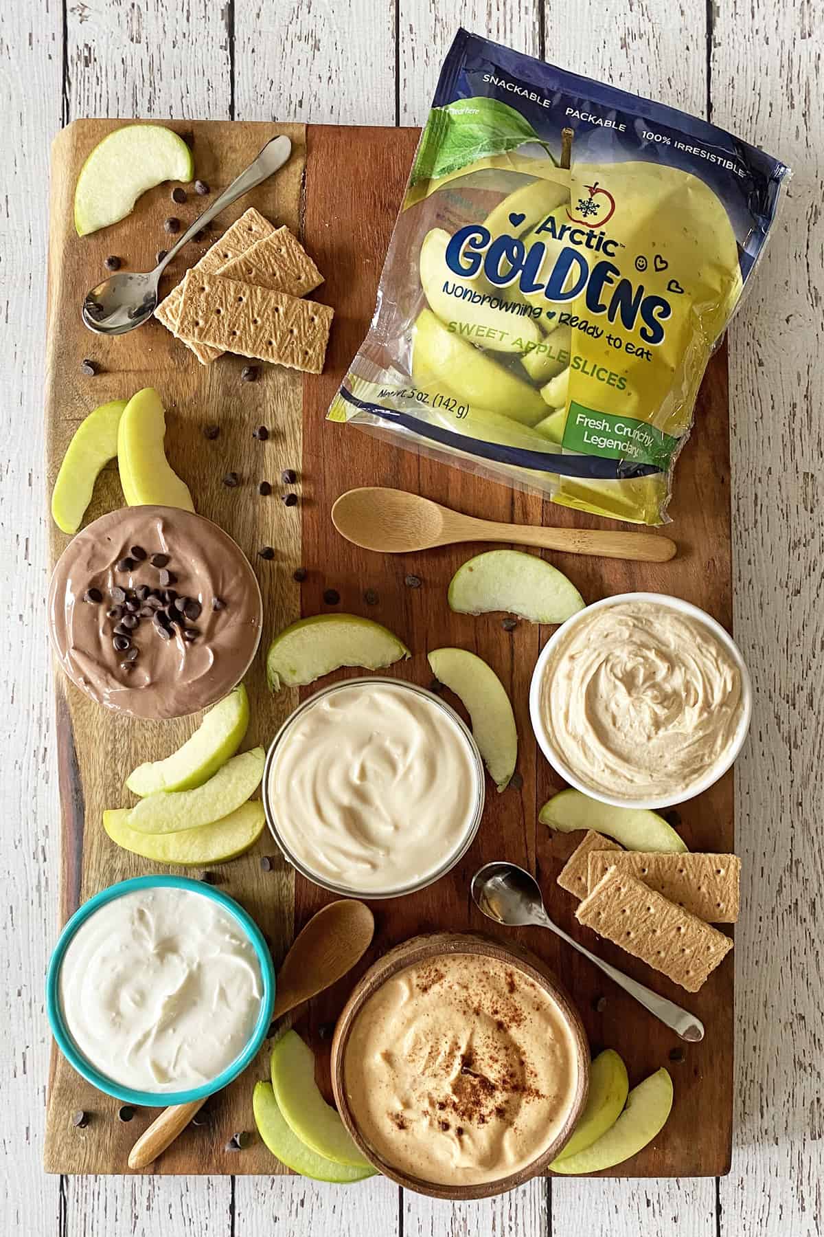 Snack board with bowls of yogurt dip, sliced apples, graham crackers and bag of sliced apples.