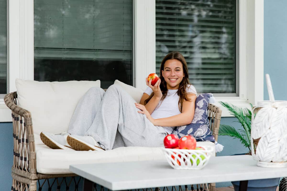 A young lady seated on a couch holding a red apple.