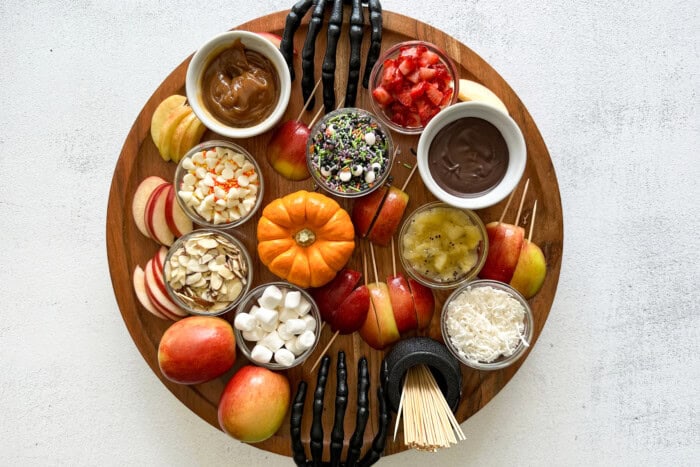 Sweet snack board with apples, toppings, and caramel, decorated with spooky skeleton hands