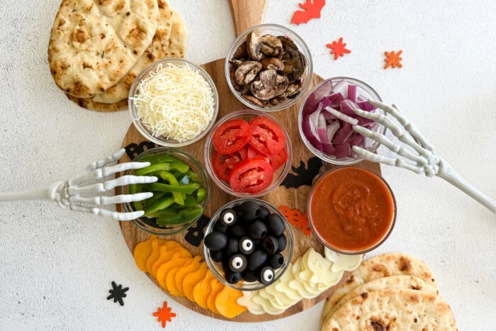Flatbreads for cooking pizza and topping ingredients decorated with skeleton hands and Halloween decor