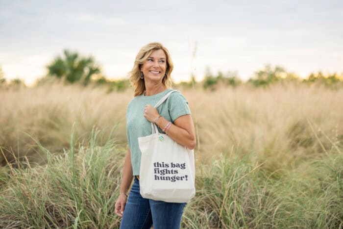A woman in a field holding her Carry the Cause tote bag.