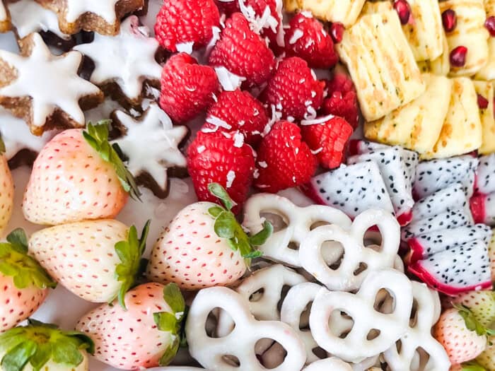 Sweet strawberries, raspberries, dragon fruit, and pretzels on a board.