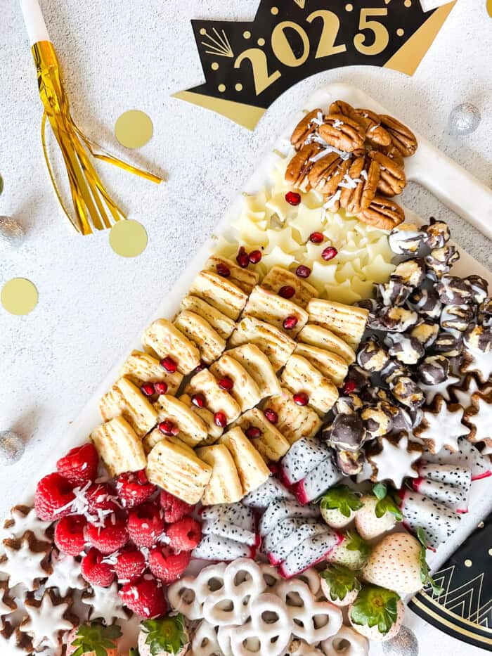 New Year's snack board with cheese, strawberries, raspberries, dragon fruit, and pretzels.