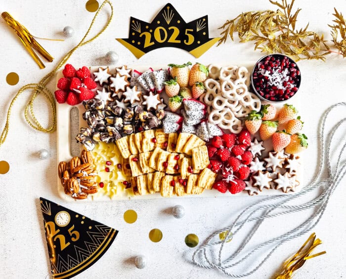 Sweet and savory snack board with New Year's decorations, including raspberries, strawberries, and nuts.